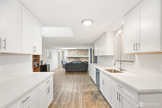 kitchen featuring stainless steel dishwasher, white cabinets, a sink, and open floor plan