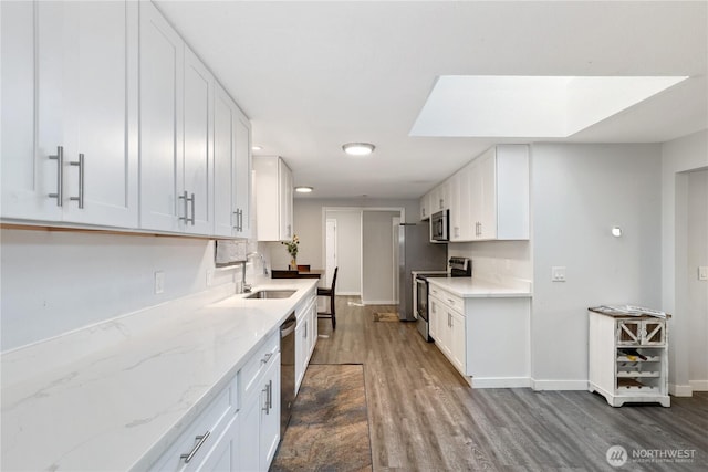 kitchen with dark wood-style floors, appliances with stainless steel finishes, a skylight, and white cabinetry