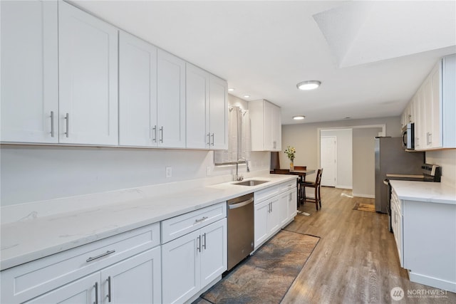 kitchen with light stone counters, appliances with stainless steel finishes, white cabinets, a sink, and wood finished floors