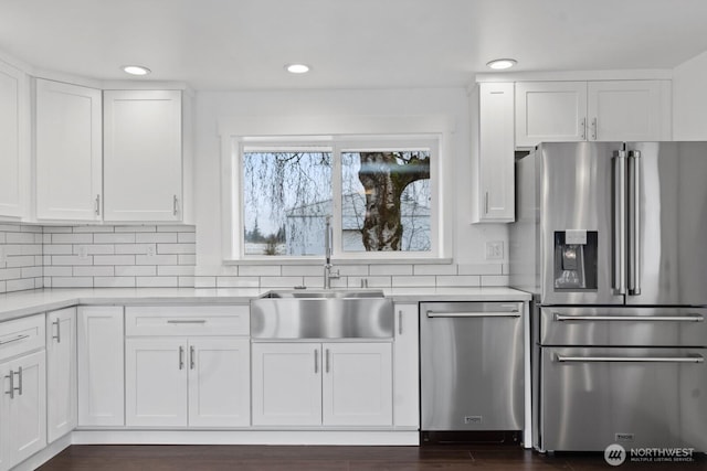 kitchen with stainless steel appliances, a sink, white cabinetry, light countertops, and decorative backsplash