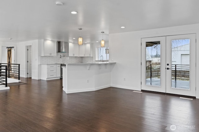 kitchen featuring french doors, tasteful backsplash, light countertops, a peninsula, and wall chimney exhaust hood