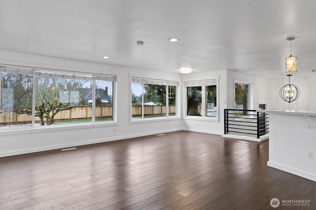 unfurnished living room featuring baseboards, dark wood-type flooring, recessed lighting, and a notable chandelier