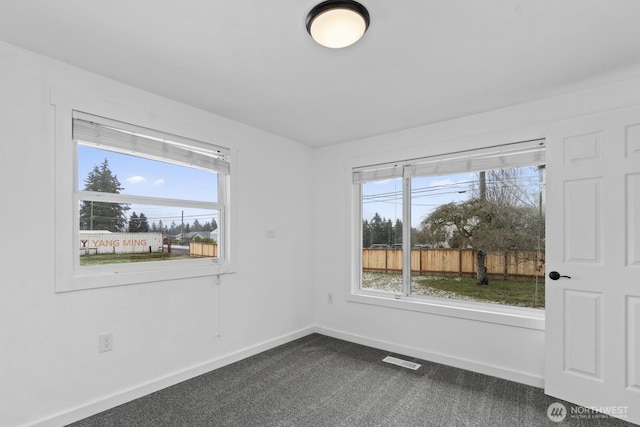 empty room featuring dark colored carpet, plenty of natural light, visible vents, and baseboards