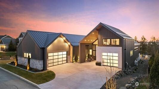 modern farmhouse with a garage, stone siding, metal roof, a standing seam roof, and board and batten siding