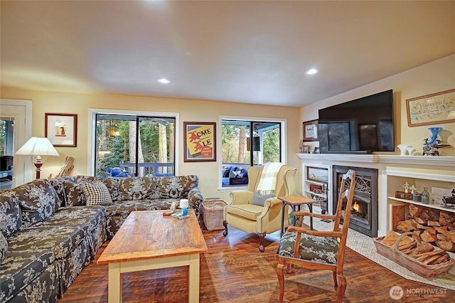 living room featuring recessed lighting, a warm lit fireplace, and wood finished floors