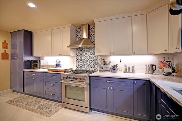 kitchen with light stone counters, white cabinets, wall chimney range hood, high end stainless steel range oven, and tasteful backsplash