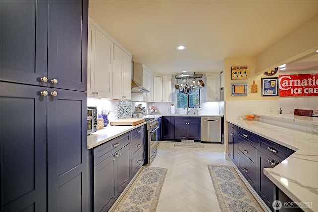 kitchen featuring white cabinets, wall chimney exhaust hood, appliances with stainless steel finishes, a sink, and backsplash