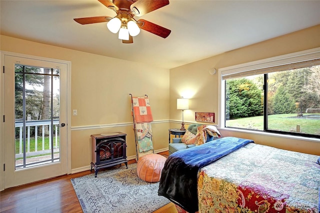 bedroom with access to exterior, a ceiling fan, a wood stove, wood finished floors, and baseboards