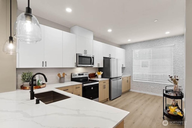 kitchen featuring hanging light fixtures, appliances with stainless steel finishes, light wood-style floors, white cabinetry, and a sink