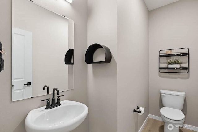 half bath featuring wood finished floors, a sink, toilet, and baseboards