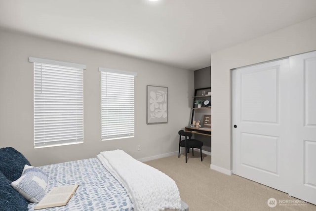 bedroom with baseboards, a closet, and light colored carpet