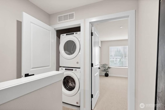 clothes washing area featuring light carpet, laundry area, baseboards, visible vents, and stacked washer and clothes dryer