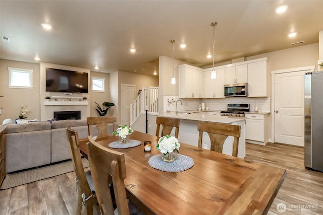 dining space featuring light wood-style floors, plenty of natural light, a fireplace, and stairway