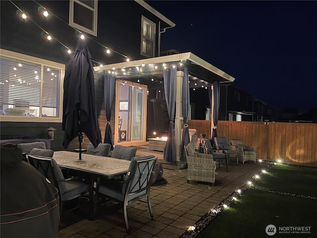 patio at night featuring outdoor dining space and fence