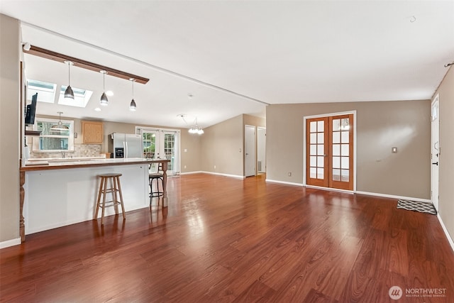 unfurnished living room with vaulted ceiling with skylight, wood finished floors, baseboards, french doors, and an inviting chandelier