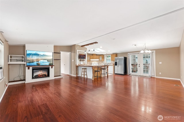 unfurnished living room featuring lofted ceiling, visible vents, a glass covered fireplace, wood finished floors, and baseboards