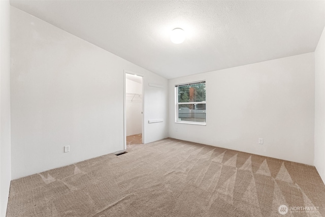 carpeted spare room featuring lofted ceiling, a textured ceiling, and visible vents