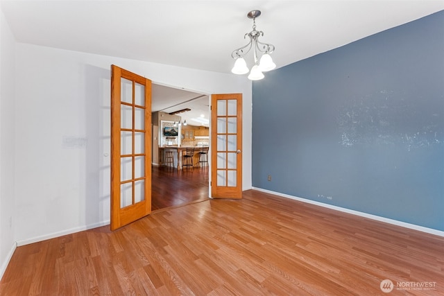 empty room with a notable chandelier, baseboards, wood finished floors, and french doors