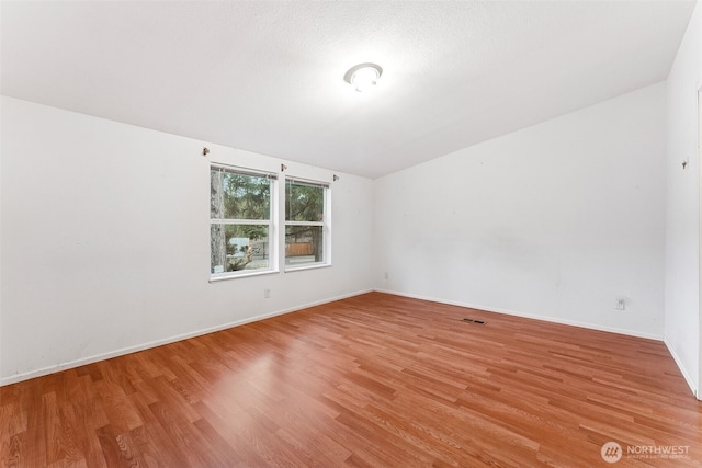 spare room featuring light wood finished floors, baseboards, and a textured ceiling