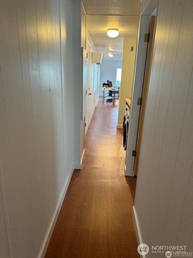 hall featuring washer / dryer, a textured ceiling, wood finished floors, and wood walls