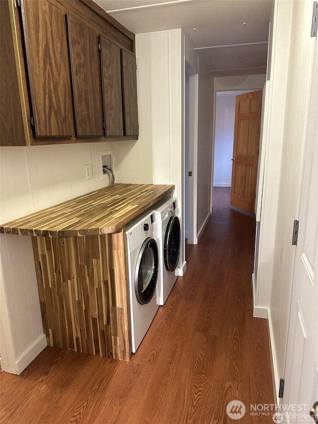 washroom featuring dark wood-type flooring, washing machine and dryer, cabinet space, and baseboards