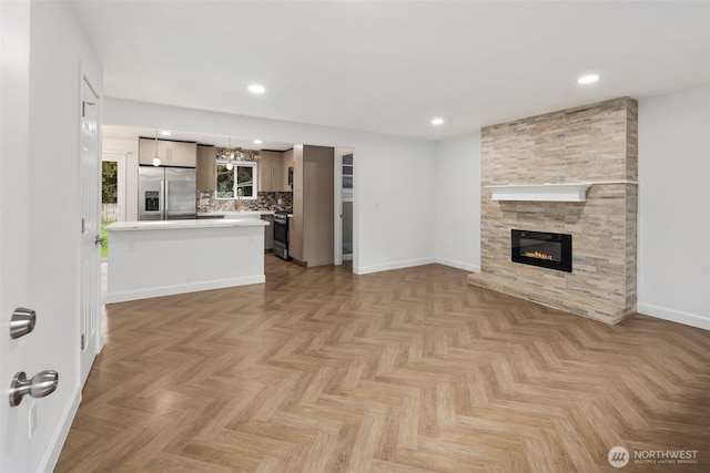 unfurnished living room featuring a chandelier, recessed lighting, a stone fireplace, and baseboards