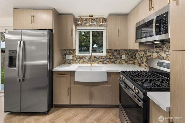 kitchen with appliances with stainless steel finishes, light countertops, a sink, and tasteful backsplash