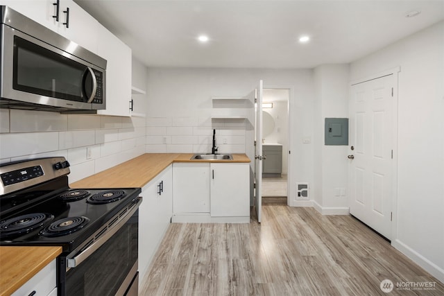 kitchen with stainless steel appliances, white cabinets, a sink, butcher block countertops, and light wood-type flooring