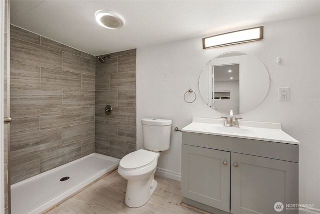 full bathroom featuring baseboards, tiled shower, toilet, wood finished floors, and vanity