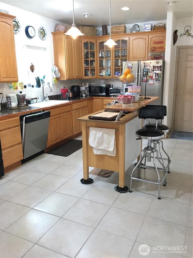 kitchen with light tile patterned floors, glass insert cabinets, appliances with stainless steel finishes, a kitchen breakfast bar, and hanging light fixtures