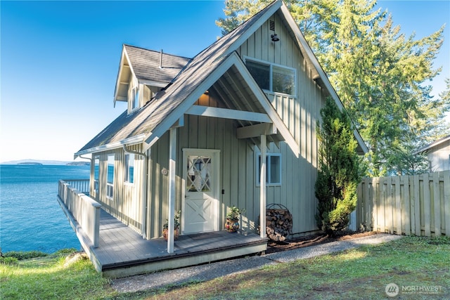 exterior space featuring fence, board and batten siding, a water view, and a shingled roof
