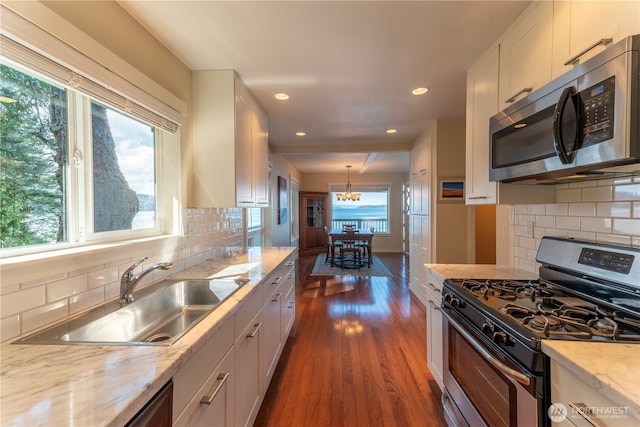 kitchen with a sink, dark wood finished floors, appliances with stainless steel finishes, white cabinets, and light stone countertops