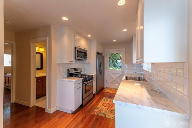 kitchen with a sink, appliances with stainless steel finishes, wood finished floors, and white cabinetry