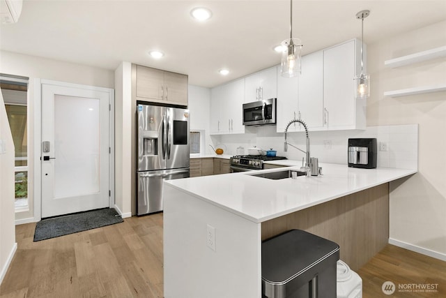 kitchen featuring stainless steel appliances, a peninsula, a sink, light countertops, and pendant lighting