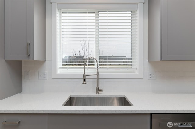 room details with dishwashing machine, gray cabinets, a sink, and light stone countertops