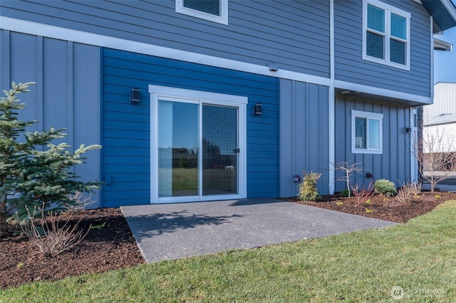 view of exterior entry with a yard, board and batten siding, and a patio