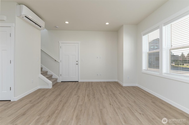 empty room with recessed lighting, baseboards, stairway, a wall mounted AC, and light wood-type flooring