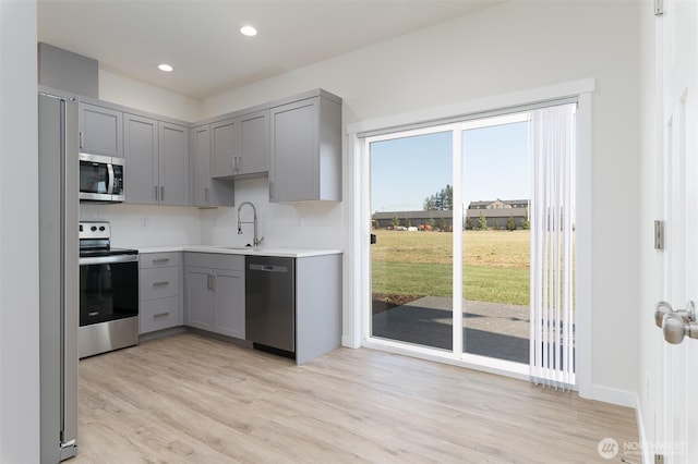 kitchen with light wood finished floors, gray cabinets, stainless steel appliances, light countertops, and a sink