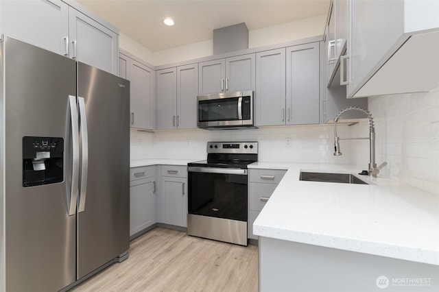 kitchen with light wood finished floors, stainless steel appliances, a sink, and gray cabinetry