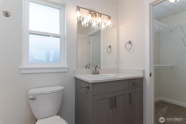 bathroom with toilet, a spacious closet, baseboards, and vanity