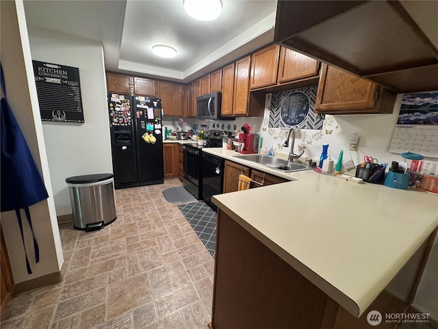 kitchen featuring black appliances, a sink, a peninsula, light countertops, and a raised ceiling