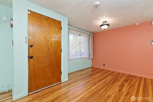 unfurnished room featuring a textured ceiling, baseboard heating, wood finished floors, and baseboards