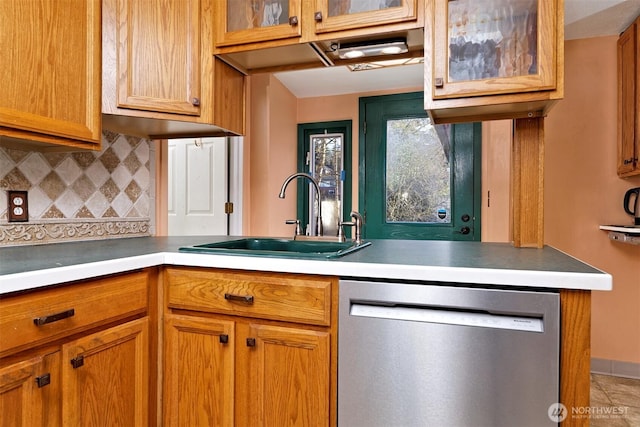 kitchen featuring decorative backsplash, glass insert cabinets, light countertops, stainless steel dishwasher, and a sink