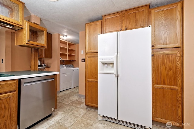 kitchen featuring white refrigerator with ice dispenser, light countertops, stainless steel dishwasher, washing machine and dryer, and a textured ceiling