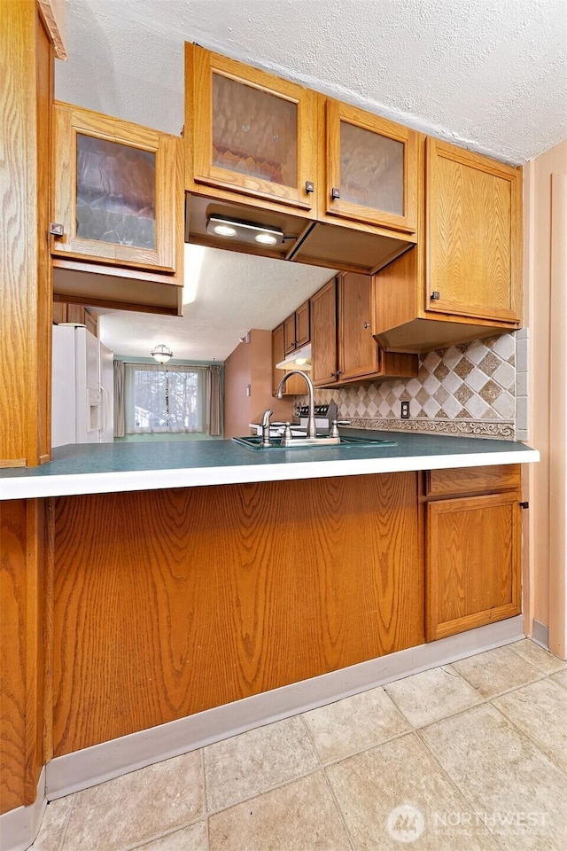 kitchen with decorative backsplash, glass insert cabinets, a textured ceiling, white fridge with ice dispenser, and a kitchen breakfast bar