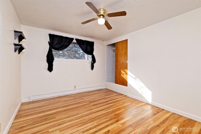 spare room with a ceiling fan, a baseboard radiator, baseboards, and wood finished floors