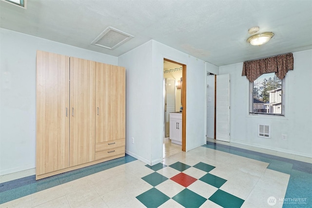 unfurnished bedroom with visible vents, attic access, a textured ceiling, baseboards, and tile patterned floors