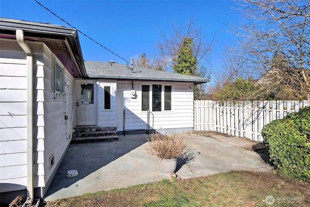 entrance to property featuring a patio, a shingled roof, and fence