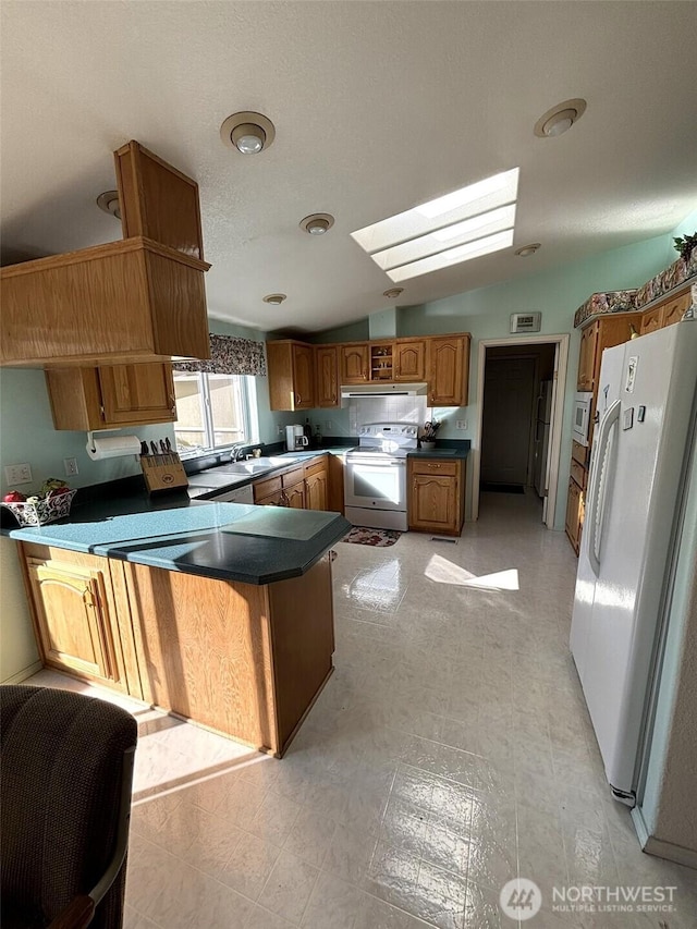 kitchen featuring dark countertops, white appliances, vaulted ceiling with skylight, a peninsula, and light floors