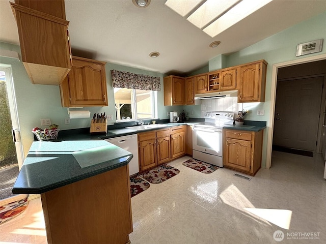 kitchen featuring visible vents, white appliances, vaulted ceiling with skylight, a peninsula, and exhaust hood